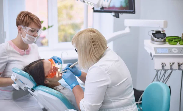 Médico dentista trata os dentes de uma bela jovem paciente. A rapariga na recepção do dentista. Médico dentista trata dente — Fotografia de Stock