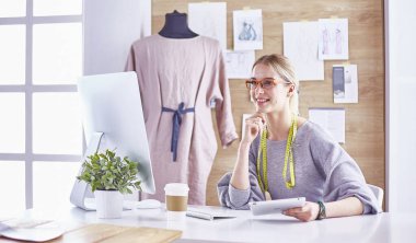 Ofiste çalışan, masaya yaslanan, çizim çeken çekici moda tasarımcısı