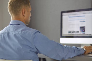 Ofiste çalışan genç işadamı, masada oturuyor, dizüstü bilgisayar ekranına bakıyor, gülümsüyor.