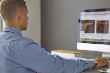 Ofiste çalışan genç işadamı, masada oturuyor, dizüstü bilgisayar ekranına bakıyor, gülümsüyor.