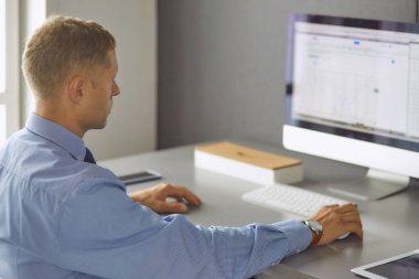 Ofiste çalışan genç işadamı, masada oturuyor, dizüstü bilgisayar ekranına bakıyor, gülümsüyor.