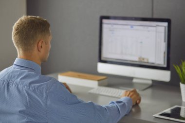 Ofiste çalışan genç işadamı, masada oturuyor, dizüstü bilgisayar ekranına bakıyor, gülümsüyor.