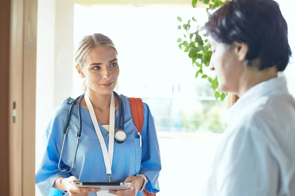 Eine junge Ärztin steht am Eingang zum Haus einer jungen Frau und ihrer kleinen Tochter — Stockfoto