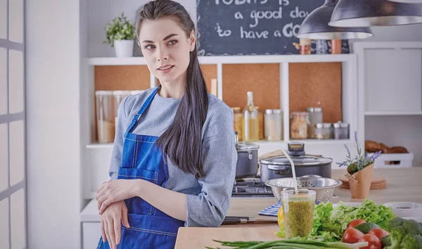 Happy young woman in kitchen with fresh vegetables on the table
