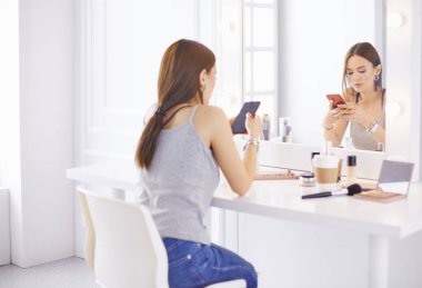 Harika bir genç kadın aynanın önünde makyaj yapıyor. Kozmetik masasının yanındaki güzel kızın portresi..