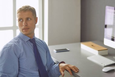 Ofiste çalışan genç işadamı, masada oturuyor, dizüstü bilgisayar ekranına bakıyor, gülümsüyor.