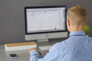 Ofiste çalışan genç işadamı, masada oturuyor, dizüstü bilgisayar ekranına bakıyor, gülümsüyor.