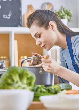 Güzel kız yemek tatma ve kit içinde pişirme sırasında gülümseyen