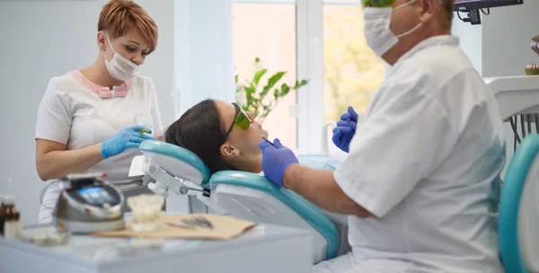 Médico dentista trata os dentes de uma bela jovem paciente. A rapariga na recepção do dentista. Médico dentista trata dente — Fotografia de Stock