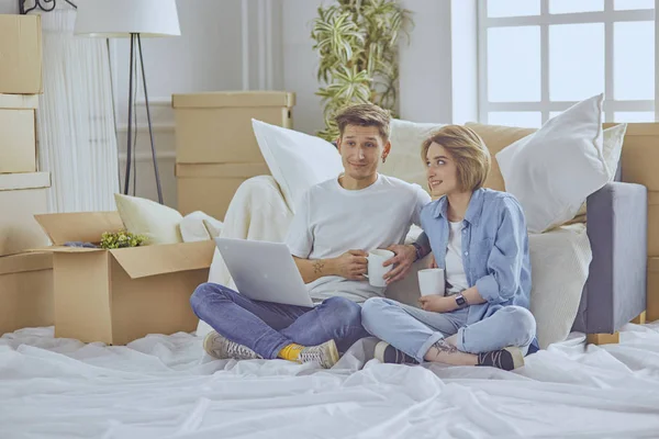 Muotokuva onnellinen pari tarkastellaan kannettavan tietokoneen yhdessä istuu uudessa talossa, ympäröivät laatikot — kuvapankkivalokuva