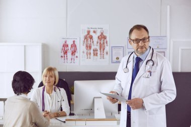 Orta yaşlı erkek doktor bir meslektaşının çalışmasına eşlik ediyor.