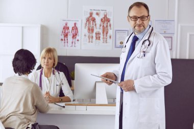 Orta yaşlı erkek doktor bir meslektaşının çalışmasına eşlik ediyor.