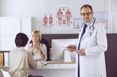 Orta yaşlı erkek doktor bir meslektaşının çalışmasına eşlik ediyor.