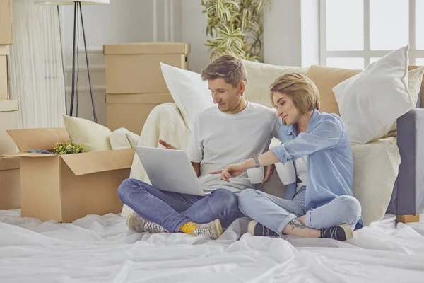 Портрет щасливої пари, дивлячись на комп'ютер ноутбука разом, сидячи в новому будинку, оточений коробками — стокове фото