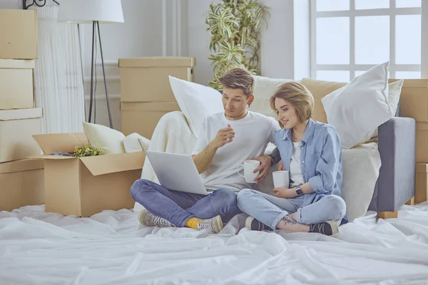 Muotokuva onnellinen pari tarkastellaan kannettavan tietokoneen yhdessä istuu uudessa talossa, ympäröivät laatikot — kuvapankkivalokuva