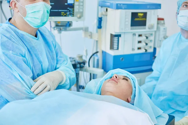 Plusieurs médecins entourant le patient sur la table d'opération pendant leur travail. Chirurgiens d'équipe au travail en salle d'opération — Photo