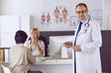 Orta yaşlı erkek doktor bir meslektaşının çalışmasına eşlik ediyor.