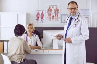 Orta yaşlı erkek doktor bir meslektaşının çalışmasına eşlik ediyor.