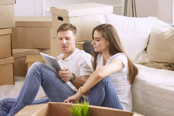 Портрет щасливої пари, дивлячись на комп'ютер ноутбука разом, сидячи в новому будинку, оточений коробками — стокове фото