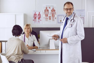 Orta yaşlı erkek doktor bir meslektaşının çalışmasına eşlik ediyor.