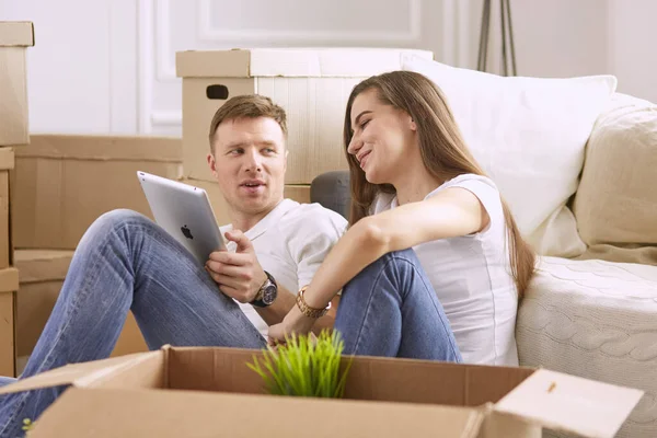 Ritratto di coppia felice guardando computer portatile insieme seduto in una nuova casa, circondato da scatole — Foto Stock