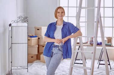 Beyaz tahta bir merdiven üzerinde güzel bir genç kadın. Odayı onarmaya hazırız. Kadın ev işi konsepti