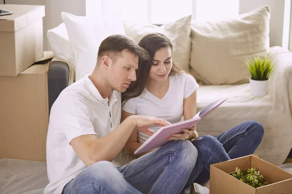 一对快乐的夫妇坐在新房子里，周围都是盒子，看着笔记本电脑的画像 — 图库照片