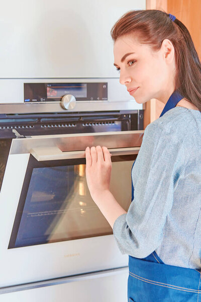 Beautiful woman in the kitchen, waiting with the front of the oven