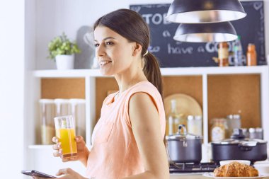 Cep telefonu görünümlü ve cam portakal suyu bir mutfakta Kahvaltı yaparken tutan gülümseyen güzel kadın