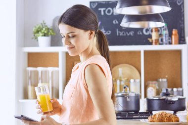 Cep telefonu görünümlü ve cam portakal suyu bir mutfakta Kahvaltı yaparken tutan gülümseyen güzel kadın