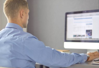 Ofiste çalışan genç işadamı, masada oturuyor, dizüstü bilgisayar ekranına bakıyor, gülümsüyor.