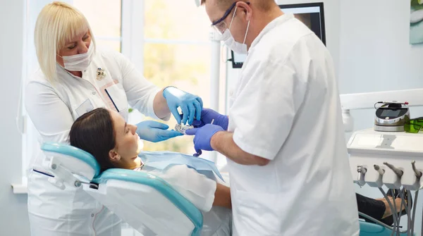 Médico dentista trata dentes de uma bela jovem paciente . — Fotografia de Stock