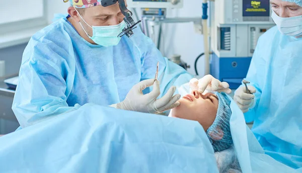 Varios médicos que rodean al paciente en la mesa de operaciones durante su trabajo. Cirujanos de equipo trabajando en quirófano — Foto de Stock