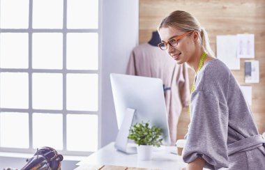 Ofiste çalışan, masaya yaslanan, çizim çeken çekici moda tasarımcısı