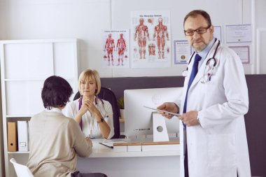 Orta yaşlı erkek doktor bir meslektaşının çalışmasına eşlik ediyor.