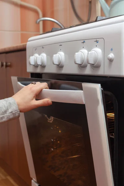 Закрыть женскую руку, открывая дверь печи, чтобы контролировать жаркое в газовой печи . — стоковое фото