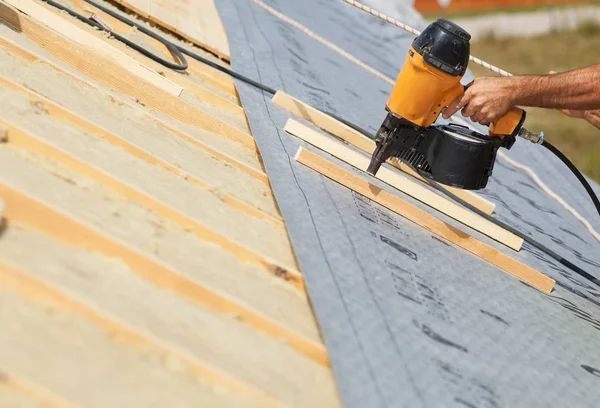 Trabalhador de empreiteiro de construção (telhados) com um prego de pistola de ar que trabalha no telhado em um novo projeto de construção de casa . — Fotografia de Stock