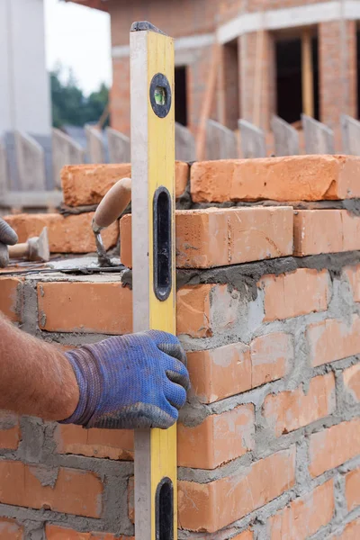 Pracownik budowlany mason pomiaru z profesjonalnym poziomie cegły na ścianach — Zdjęcie stockowe