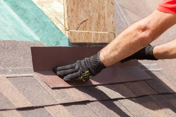 Roofer builder worker installing shingles on a new wooden roof with skylight . — Stock Photo, Image