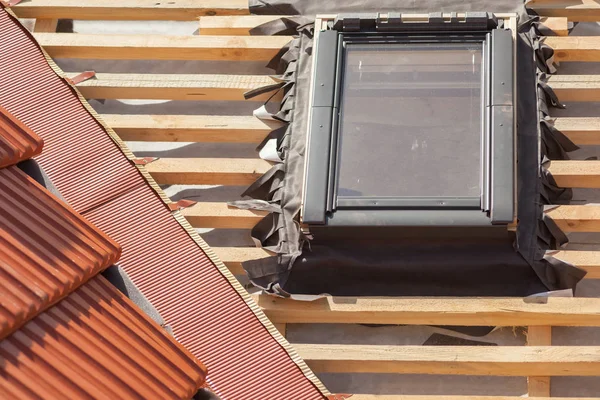 Nieuw dak in aanbouw met houten balken, waterproofing laag voor hoek, dakraam en natuurlijke tegel. — Stockfoto