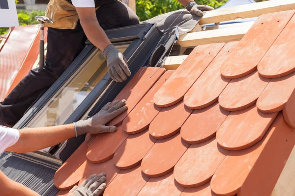 Manos de tejado colocando baldosas en el techo. Instalación de baldosas rojas naturales. Techo con ventanas de mansarda —  Fotos de Stock