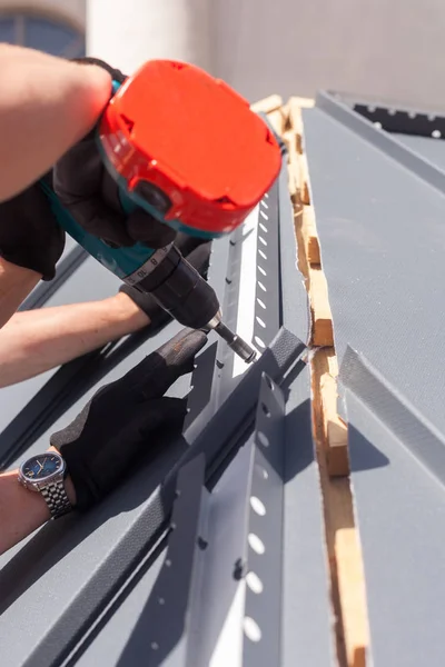 Arbeiter auf einem Dach mit Elektrobohrmaschine installiert Metallziegel auf Holzhaus. — Stockfoto