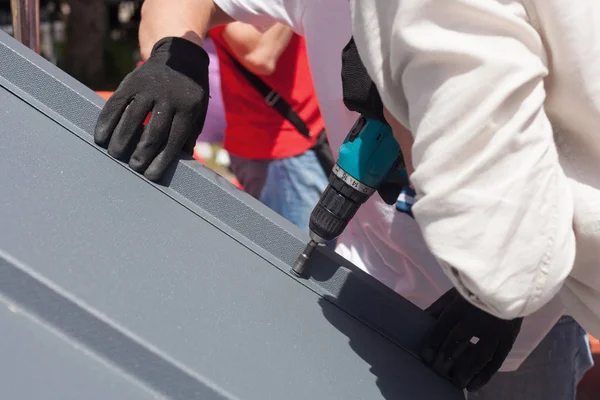 Worker on a roof with electric drill installing metal tile on wooden house. — Stock Photo, Image