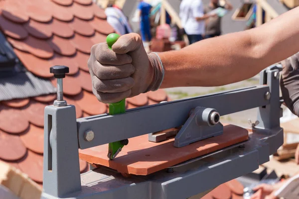 Roofer construtor trabalhador usar cortador de telha para criar um tamanho correto de telha cerâmica vermelha natural . — Fotografia de Stock