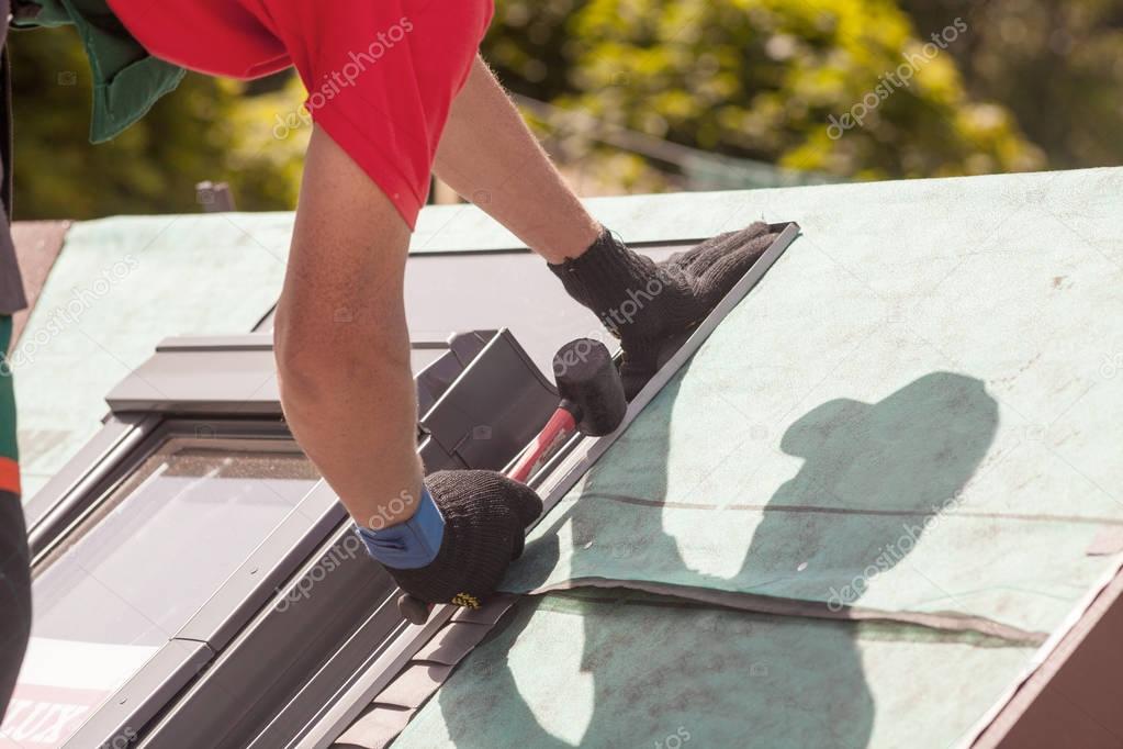 Roofer installs metal profile on a roof window with a rubber mallet.