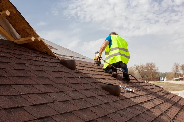 Construction worker putting the asphalt roofing (shingles) with nail gun on a large commercial apartment building development. — Stock Photo, Image