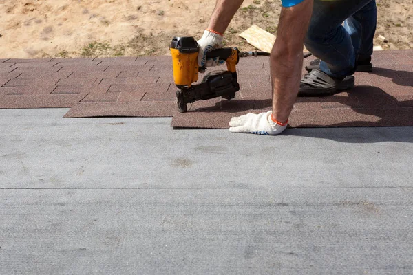 Roofer constructor trabajador con pistola de clavos instalación de tejas de asfalto o baldosas de betún en una nueva casa en construcción . — Foto de Stock