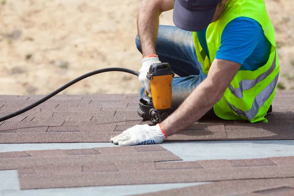 Pokrývač tvůrce pracovník s nailgun instalace asfaltové šindele nebo Asfaltové dlaždice na nový dům ve výstavbě. — Stock fotografie