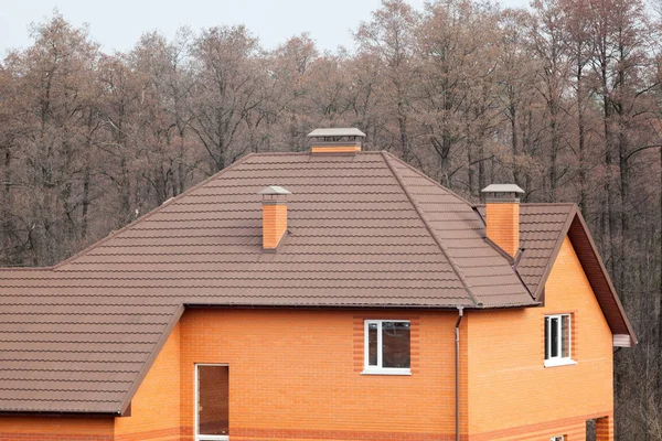 Nueva casa de ladrillo con chimenea modular, baldosas de techo de metal recubierto de piedra, ventanas de plástico y canalón de lluvia . — Foto de Stock