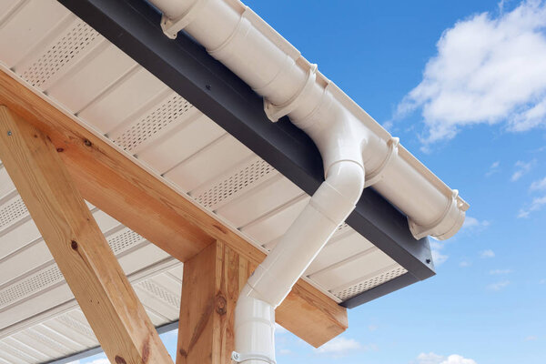 SIP panel house construction. New white rain gutter.  Drainage System with Plastic Siding Soffits and Eaves against blue sky.